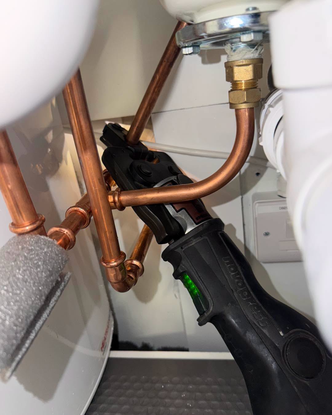 Copper pipework being pressed under a sink during an installation