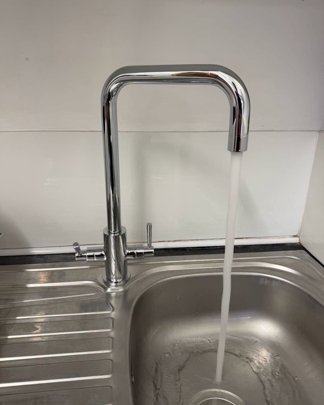 A chrome kitchen tap running into a stainless steel sink